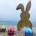 Osterhase aus Holz, bunte Eier drumherum im Sand, Meer Im Hintergrund